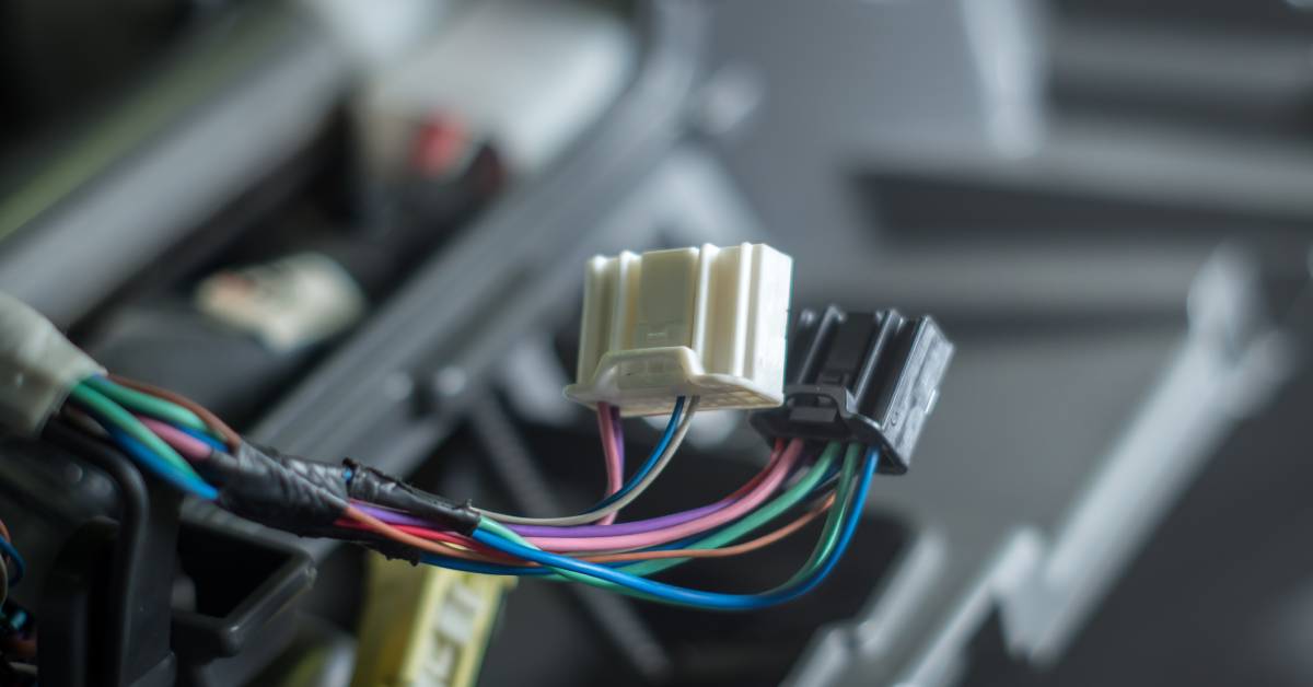 A black and a white rectangular connector with red, blue, and green wires threaded through it to power electric systems.